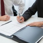 A Person in Black Suit Holding a Pen Near the Documents on the Table